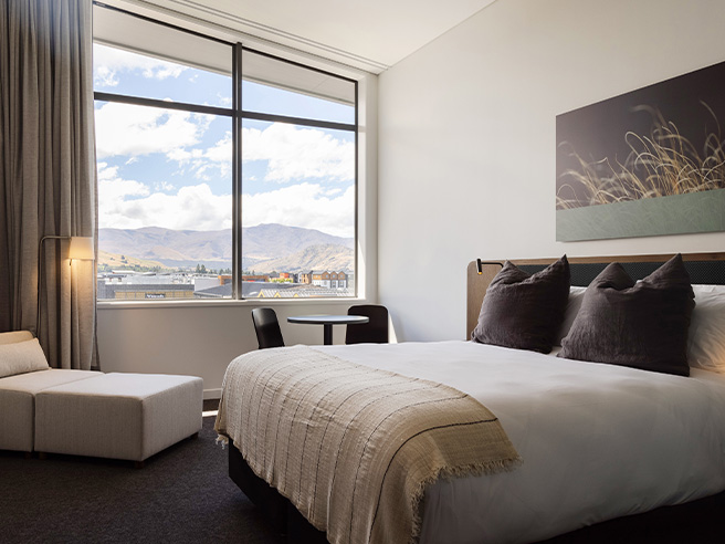 Spacious hotel room with large windows, ocean view, and mountain backdrop